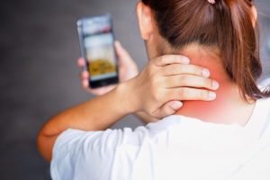 Donna che si tocca il collo per il dolore mentre osserva il cellulare